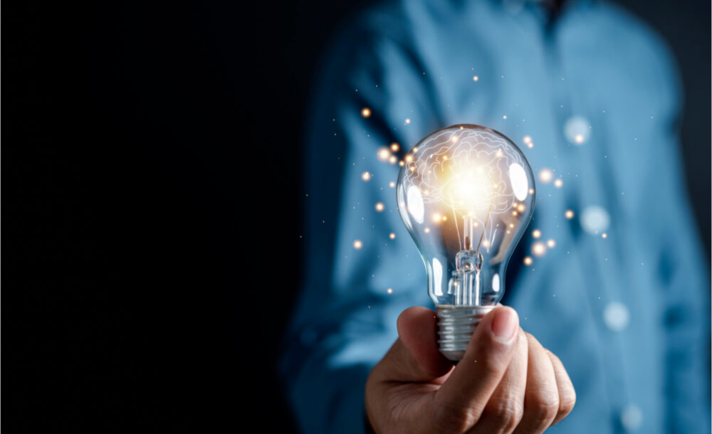 A person in a blue shirt holds a glowing light bulb.